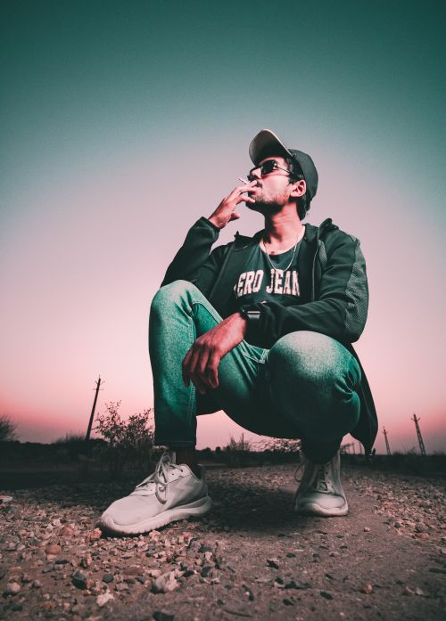 Free Young man in casual attire smoking outdoors at dusk, capturing urban lifestyle vibes. Stock Photo
