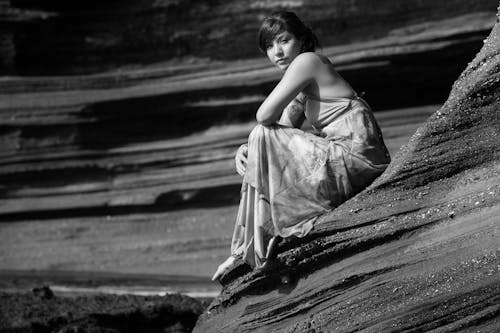 Grayscale Photo of a Woman Sitting on a Rock