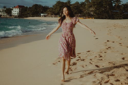 Free A Woman in Floral Dress Walking in the Beach Stock Photo