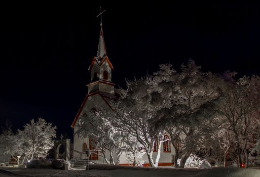 在冰岛晴朗的夜空下，一座风景如画的教堂被白雪覆盖的树木包围着