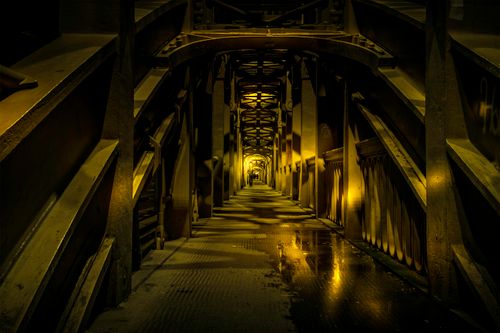 Free Eerie view inside a steel tunnel with reflections on puddles under dim lighting. Stock Photo