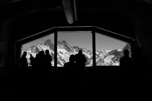 Silhouetted figures admire the stunning view of snow-capped mountains through a large window in Lauterbrunnen, Switzerland.