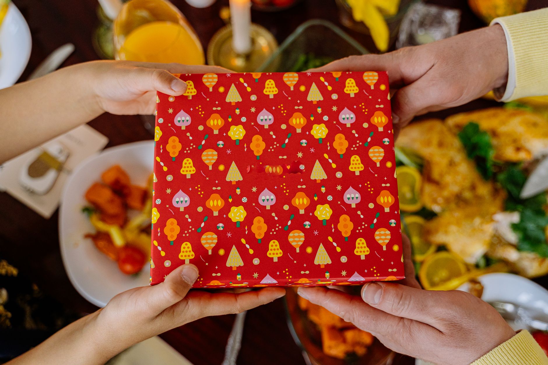 Close-up of wrapped gift being exchanged over a holiday dinner table, capturing the festive spirit.