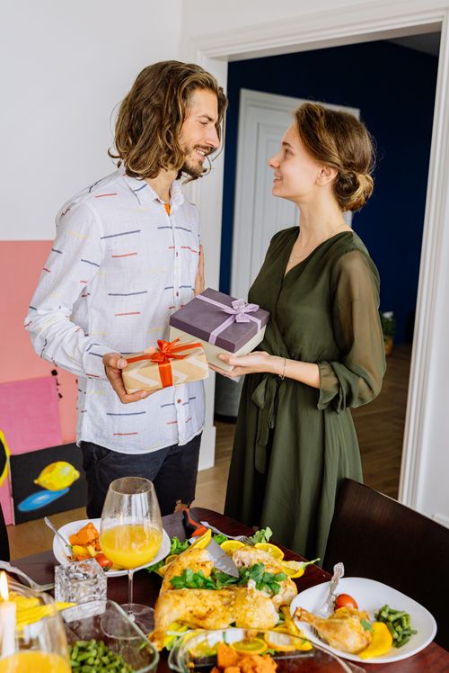 Free A happy couple exchanges gifts while standing near a festive meal indoors. Stock Photo