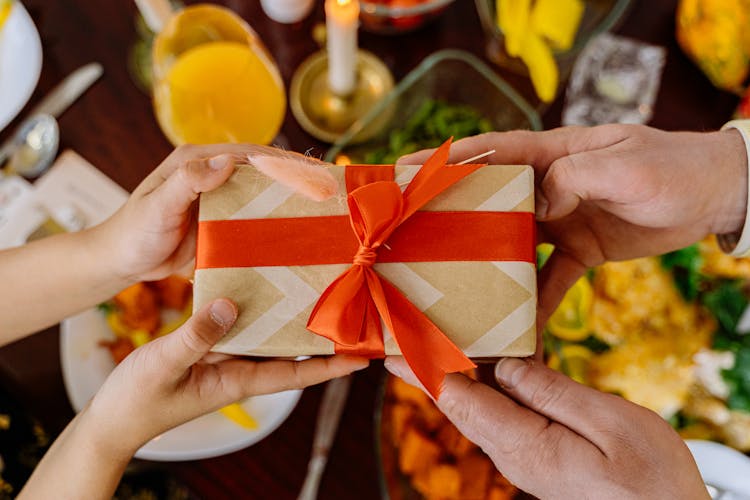 Close-Up Shot Of Two People Holding A Wrapped Gift With A Ribbon