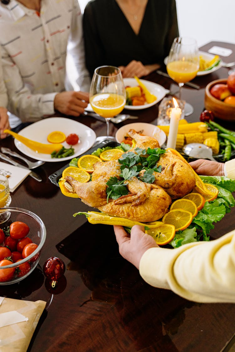 A Person Serving A Sliced Fried Chicken With Lemon Slices And Green Leaves