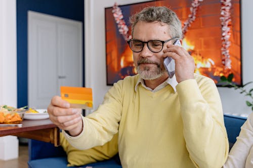 Free An Elderly Man Looking at a Card Holding a Cellphone to His Ear Stock Photo