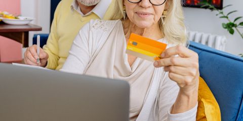 Elderly couple smiles as they shop online with a credit card on a cozy couch.