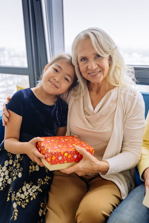 Free A heartwarming moment of a grandmother and granddaughter sharing a gift indoors. Stock Photo