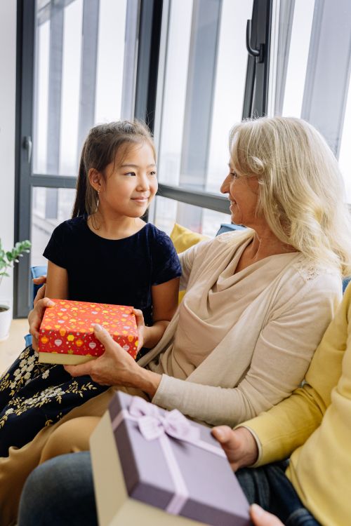 Free A joyful moment of a grandmother and granddaughter exchanging gifts indoors. Stock Photo