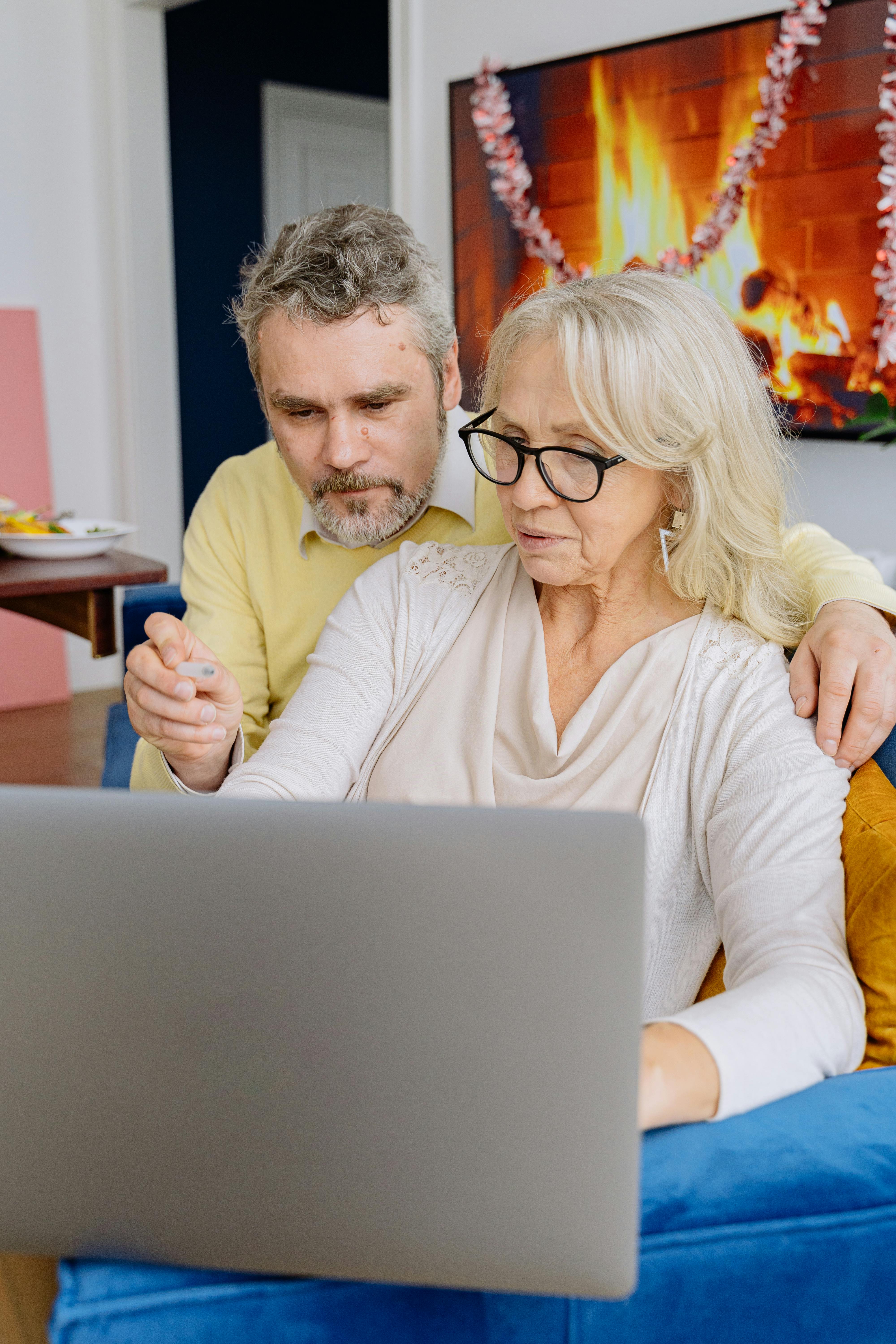 an elderly couple sitting on a couch using laptop