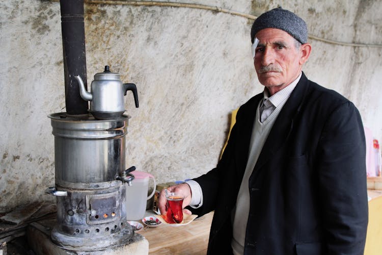 Ethnic Man With Glass Of Tea Near Old Stove