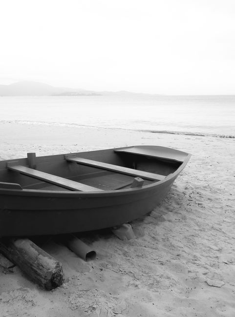 A serene grayscale scene features a wooden boat resting on a tranquil sandy beach.
