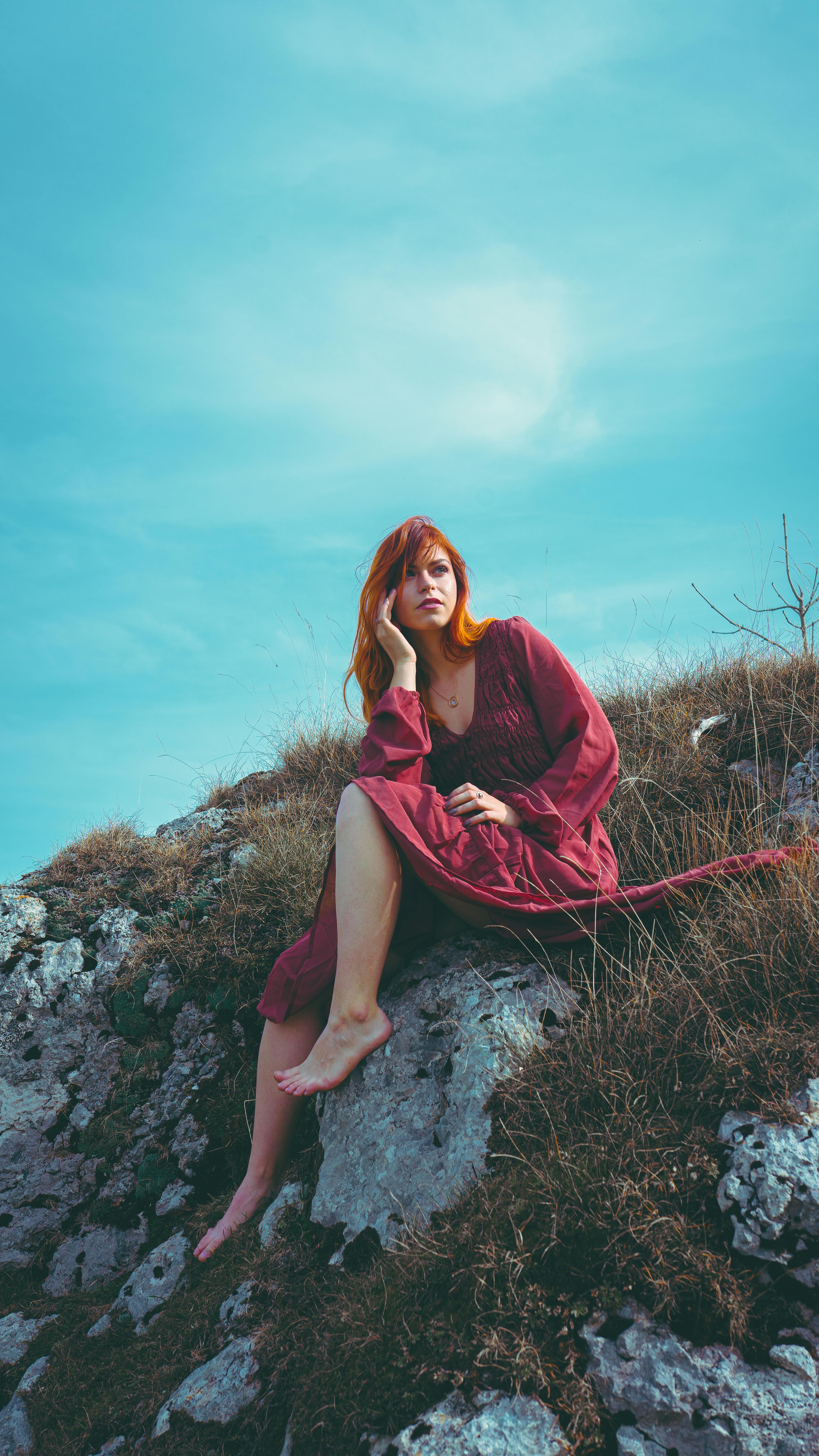 stylish woman sitting on rocky cliff