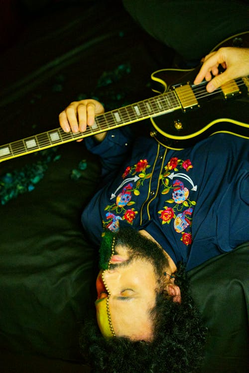 Man in Blue Shirt Playing Guitar While Lying on Bed