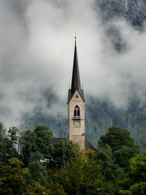 Free Chapel Spire Among Trees in Clouds Stock Photo