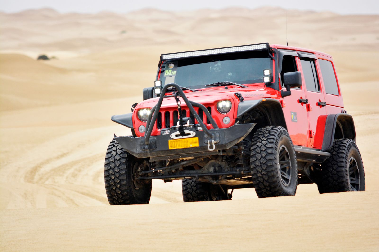Lifted red Jeep Wrangler with a front winch driving across open, treeless desert sand dunes with no anchor points in sight