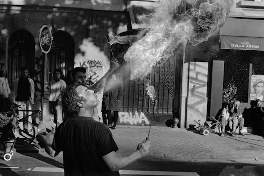Black and white of confident male acrobat blowing fire during show on city street