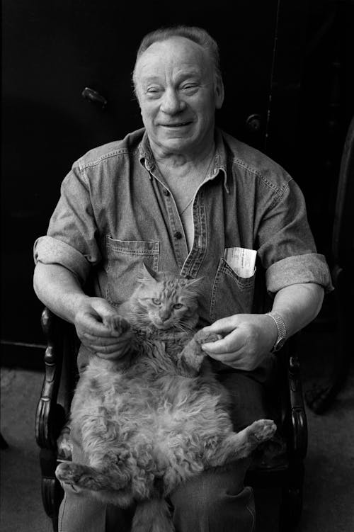 Aged male in casual outfit sitting on chair and playing with domestic cat