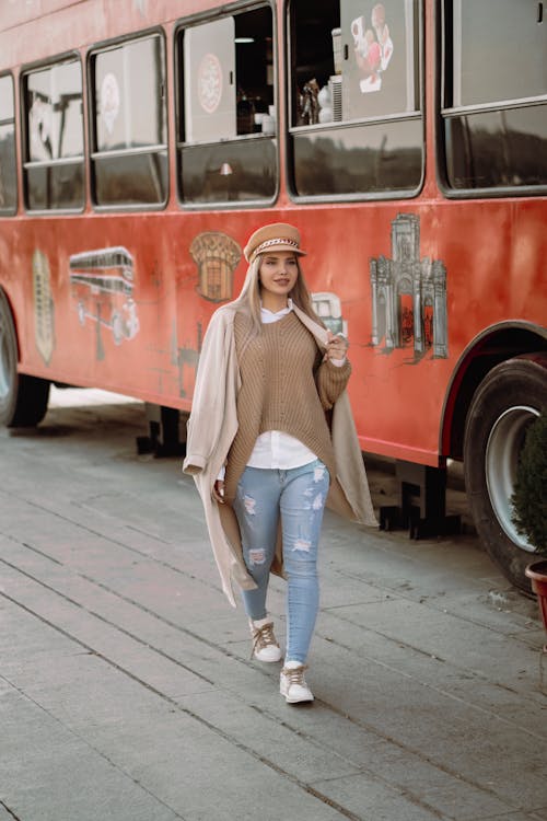 Woman in Beige Knit Sweater Walking Beside Red Bus