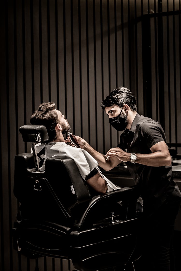 Man In Sitting On Black Leather Chair During Beard Haircut