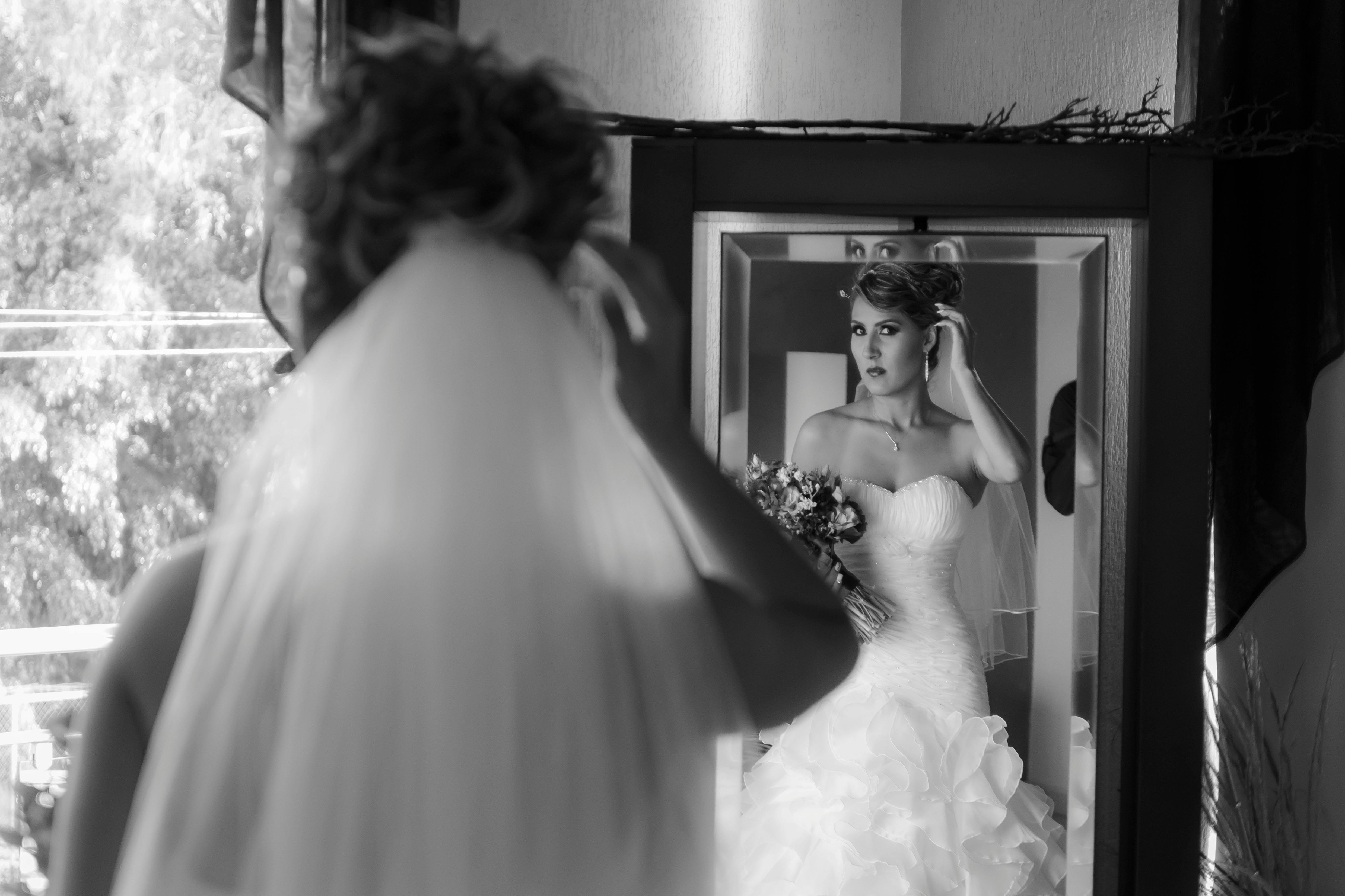 A beautiful bride in gown and veil checks her reflection in a mirror, preparing for the wedding ceremony.