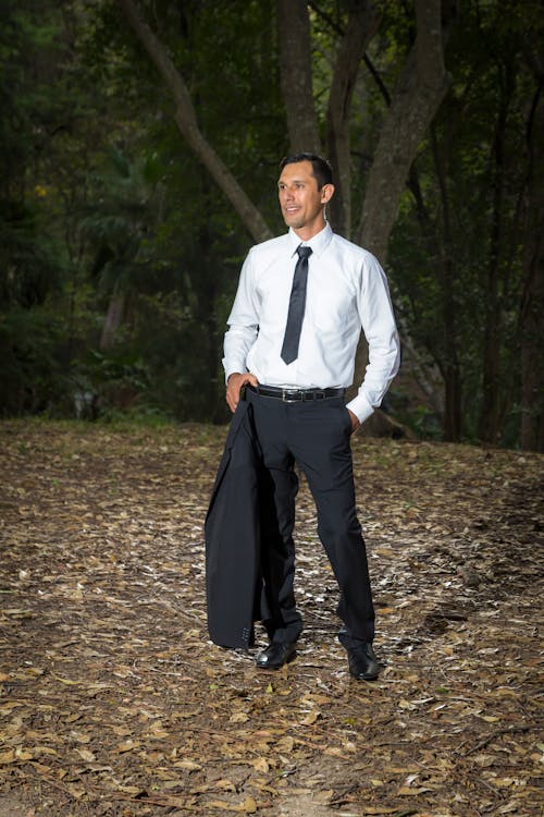 Man in White Shirt and Black Suit Standing on Dried Leaves