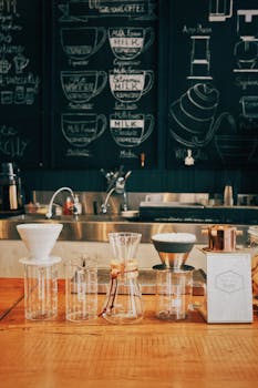 Glass bottles with various types for brewing coffee placed on table with menu and sink on background in cafe