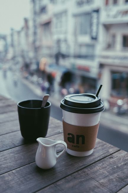 Cup of drink and takeaway mug placed on wooden counter in street cafe in daytime