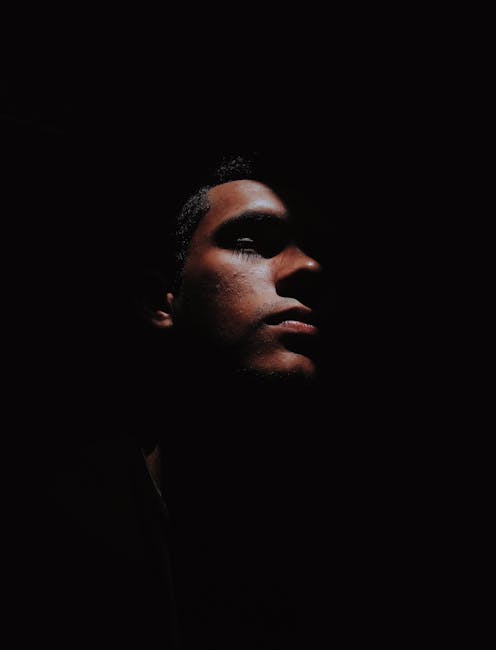 Dramatic side-profile portrait of a man with dark shadows and moody lighting.