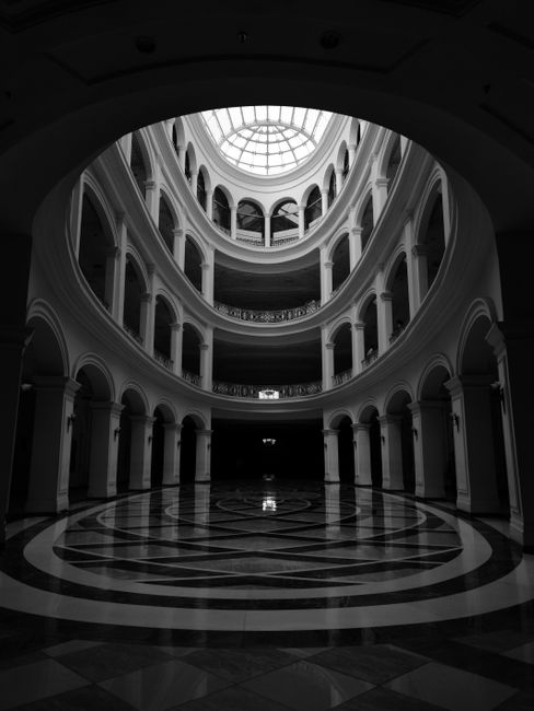 Dramatic black and white view of a grand historical building's interior with elegant arches and domed ceiling.