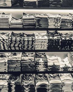 Black and white image showcasing neatly folded t-shirts stacked on store shelves.