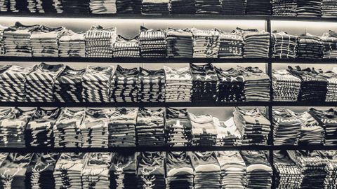 Black and white image showcasing neatly folded t-shirts stacked on store shelves.