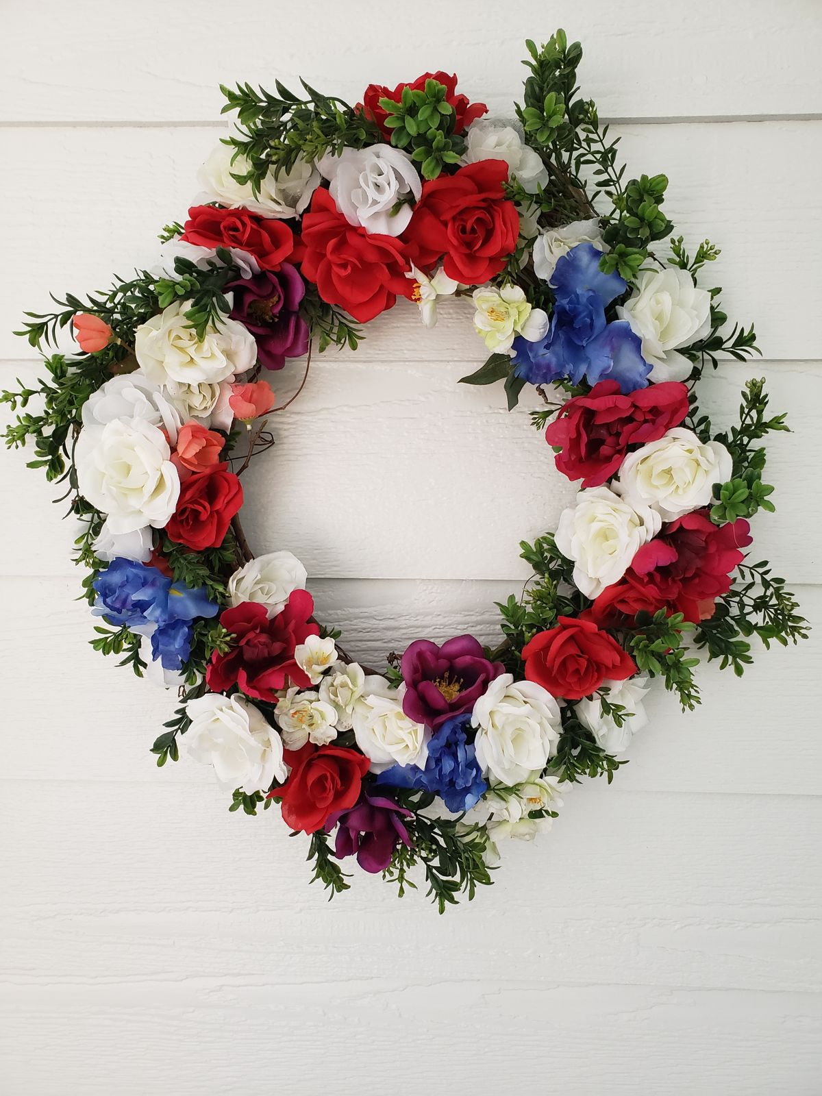 A vibrant floral wreath featuring red, white, and blue flowers on a white wall. Stock Photo.