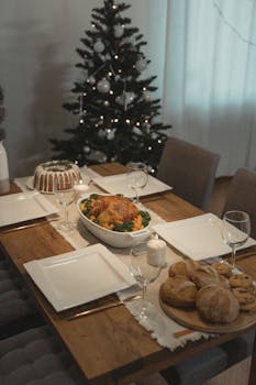A festive holiday dining table featuring a roast turkey, bread, and Christmas tree.