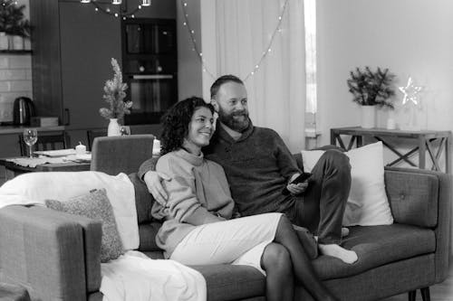 Free A Grayscale Photo of a Couple Watching TV on the Sofa Stock Photo