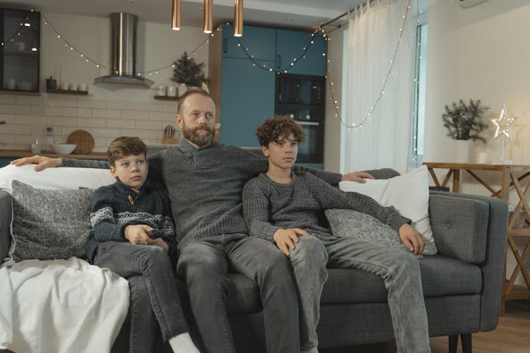 A Father And His Children Watching TV On A Sofa