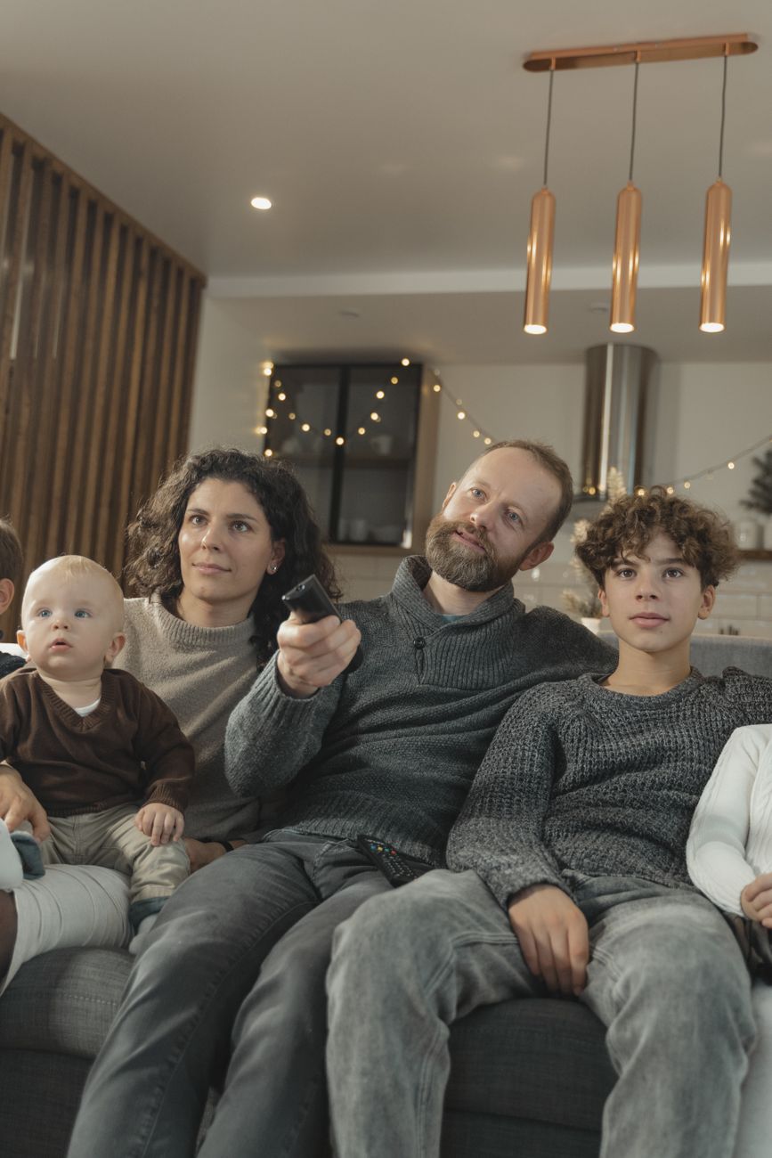 A family on the sofa watching television together, the ideal version of children's TV as a shared room rather than a stream of fragments.