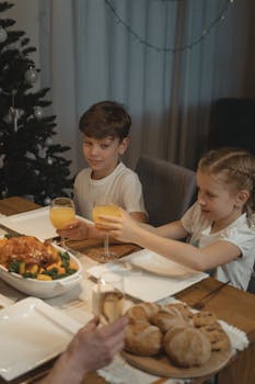 Two kids seated at a festive dinner table, sharing a meal with roast chicken and orange juice.
