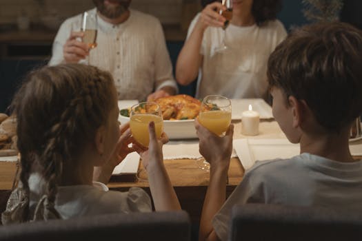 Two children and adults together at a cozy family dinner table, raising glasses in a toast.