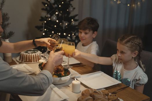 Family enjoying a cozy Christmas dinner with children toasting in a festive setting.
