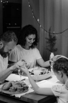 A family of three holds hands and prays at a festive Christmas dinner table indoors.