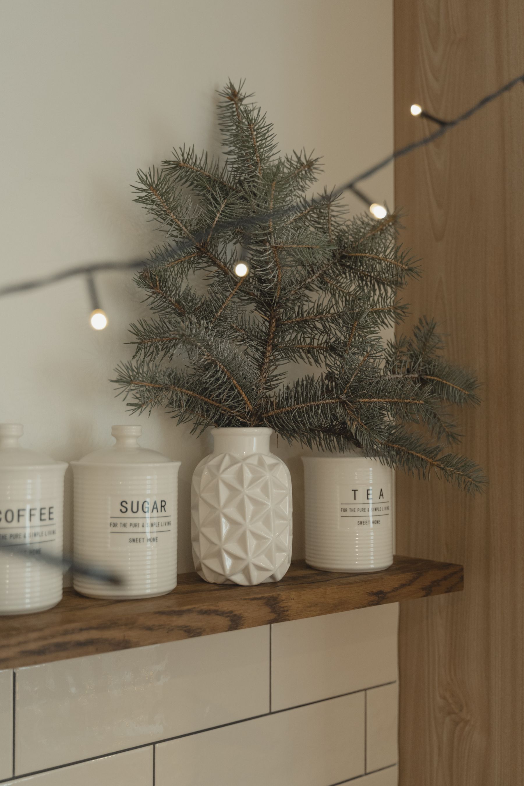Ceramic kitchen jars styled with pine branches and warm Christmas lights