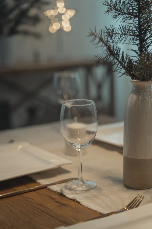 Free A beautifully set table with a ceramic vase, pine branches, and wine glass, creating a cozy festive mood. Stock Photo