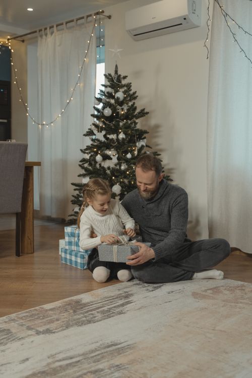 Free A father and daughter joyfully unwrap gifts beside a decorated Christmas tree indoors. Stock Photo
