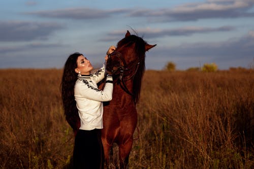 Woman caressing horse in grassy meadow in countryside
