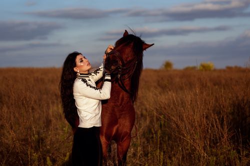 Free Side view of female with long hair standing near horse in meadow in village Stock Photo