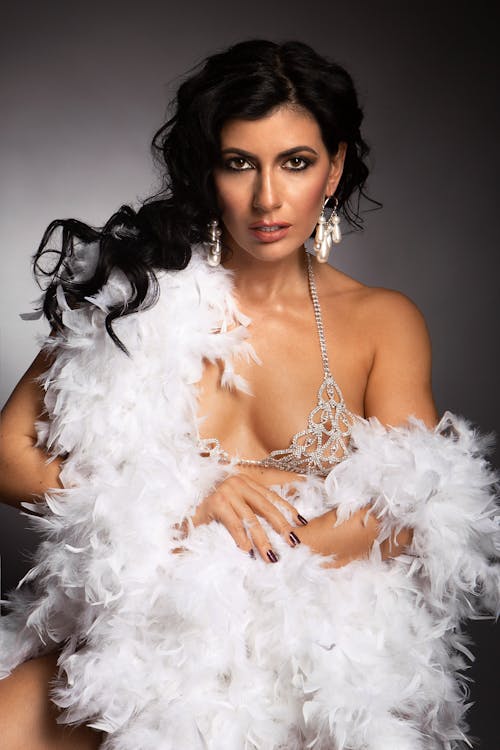 Confident female in bra decorated with shiny gems wrapped in feather boa looking at camera