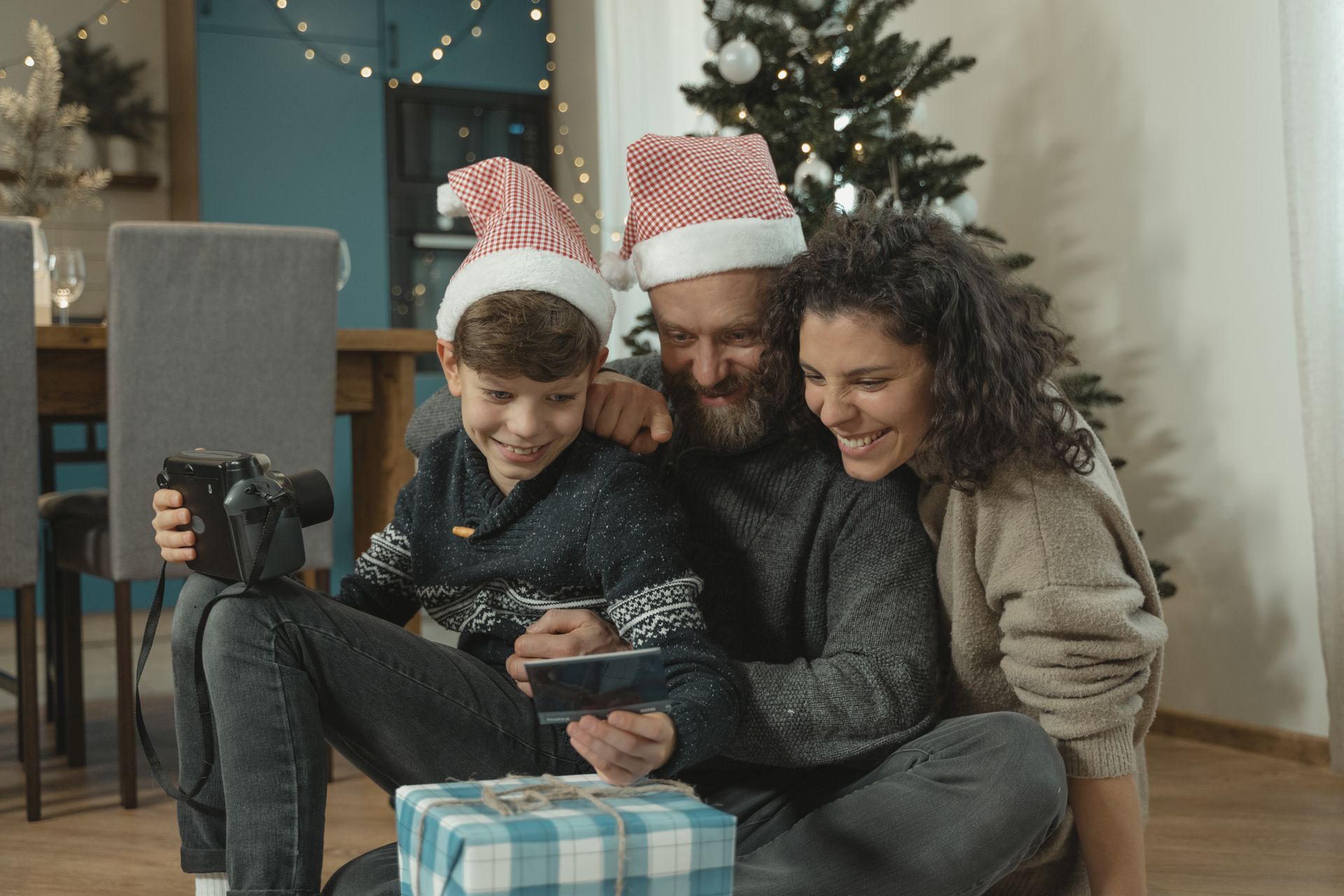 Family enjoying Christmas together with technology and gifts by the tree.