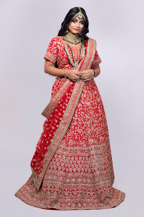 Full body of female in authentic Indian bridal dress and jewelries standing in studio against gray background
